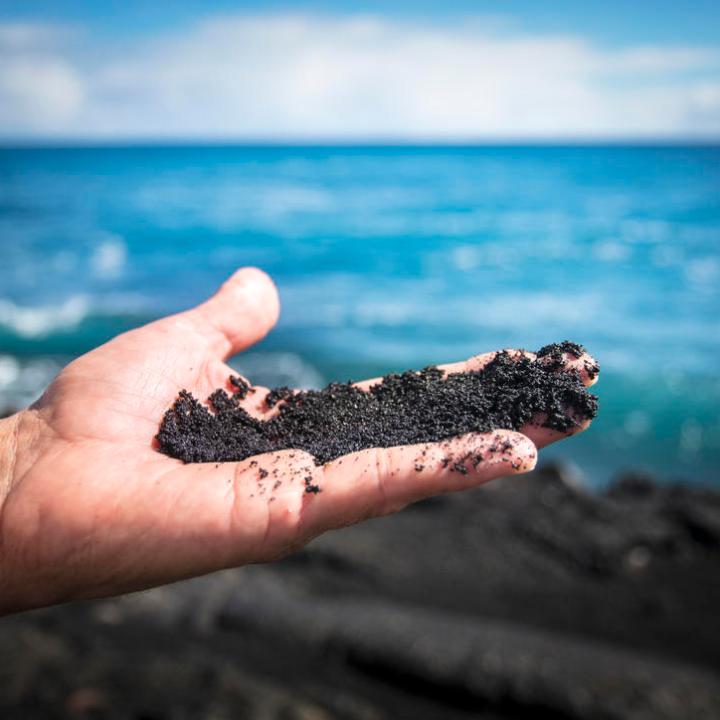 a hand holding a water bottle next to a body of water